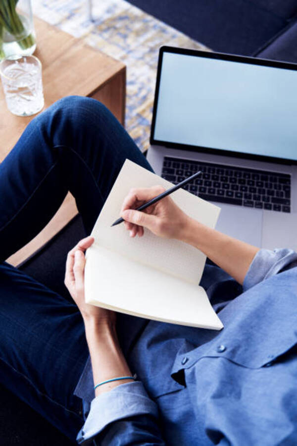 一位成年人坐在办公桌前，双臂伸向头顶做轻柔伸展，桌上有笔记本电脑和笔记本